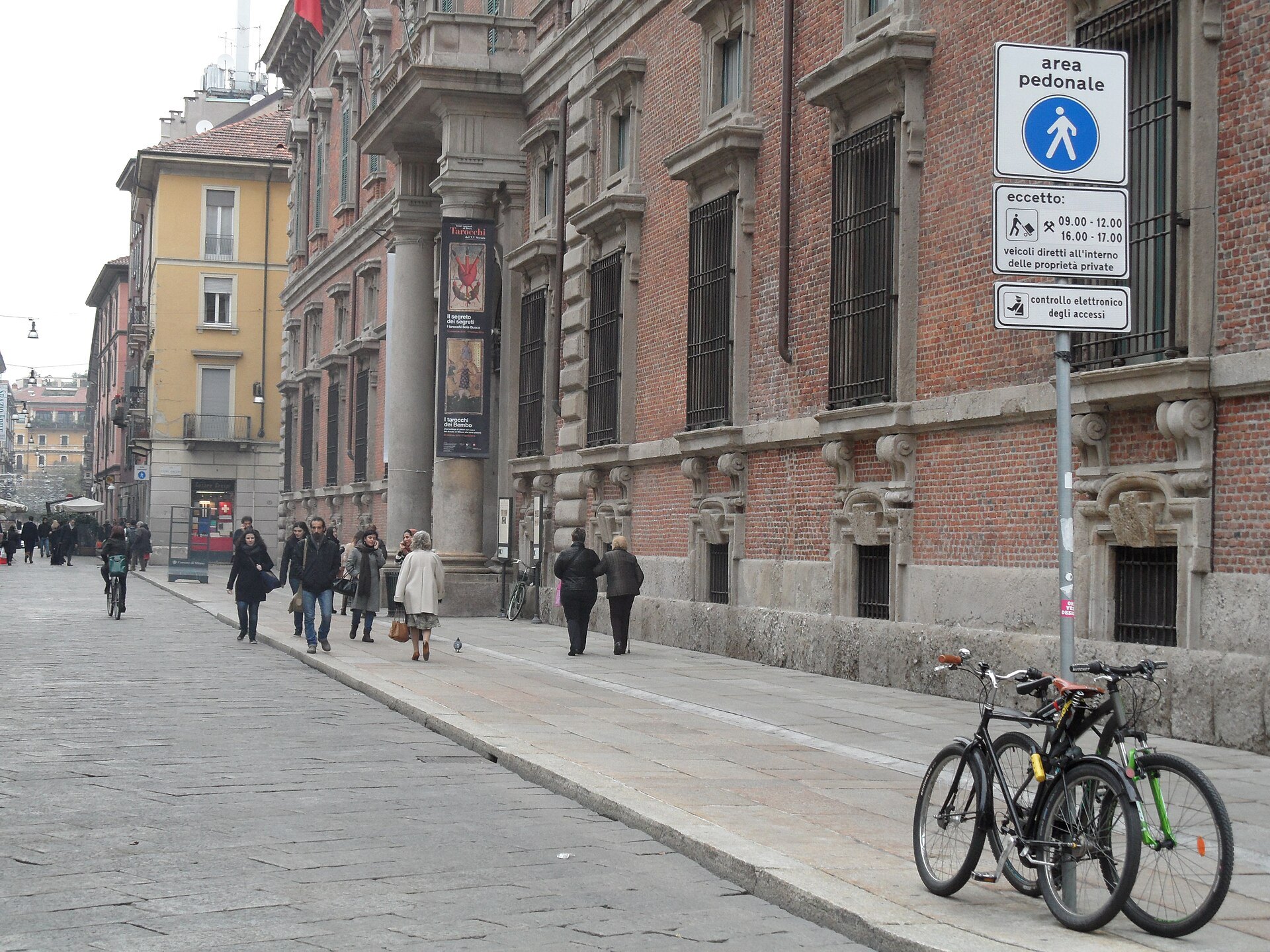 A Brera street with bicycles against the kerb and people walking towards the palazzo