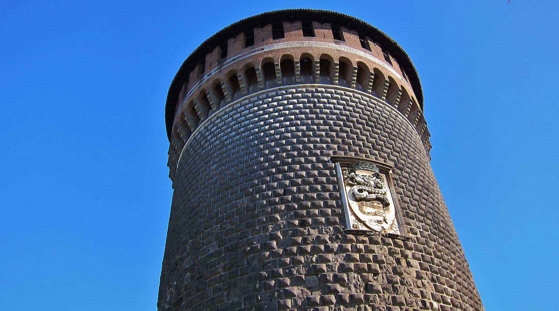 The castle's round brick tower seen from directly below against a blue sky