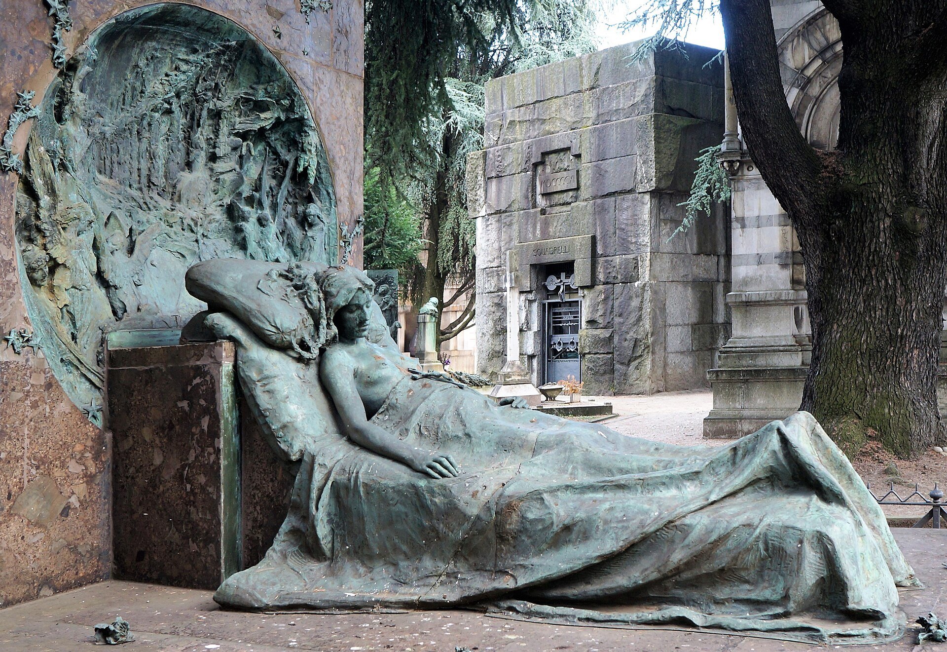 A reclining bronze funerary figure against a granite tomb wall