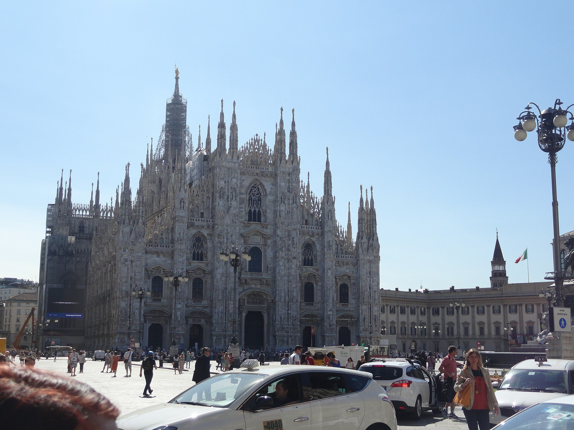 The cathedral seen at an angle from across the square, cars and people in front of it