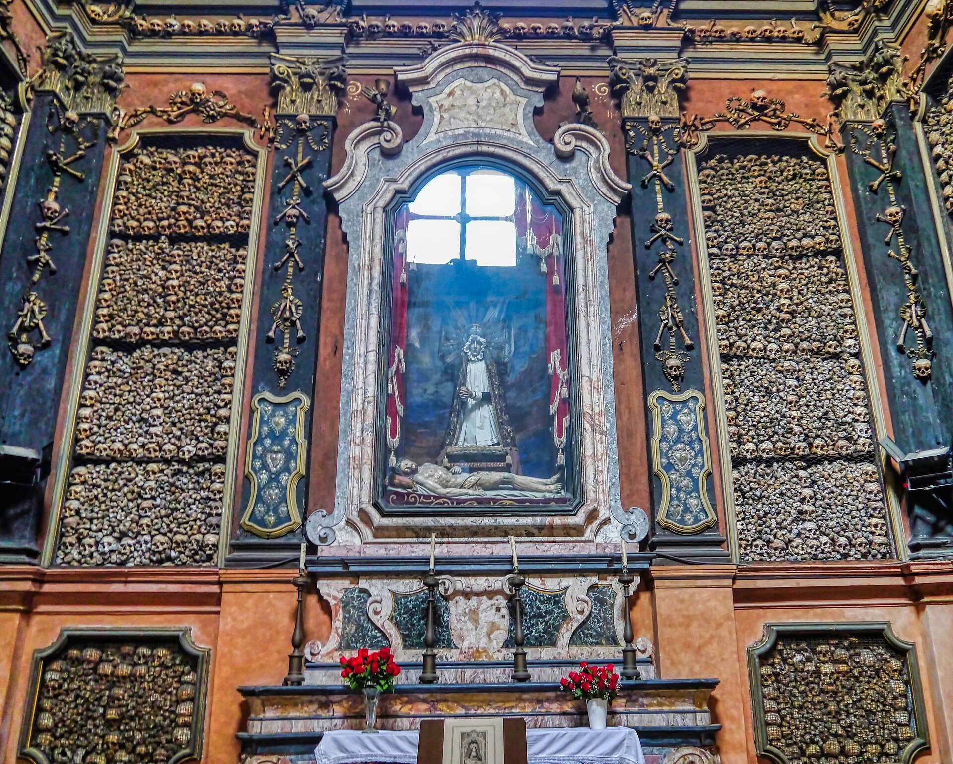 The ossuary chapel of San Bernardino, its walls lined floor to ceiling with human bones around a lit altar