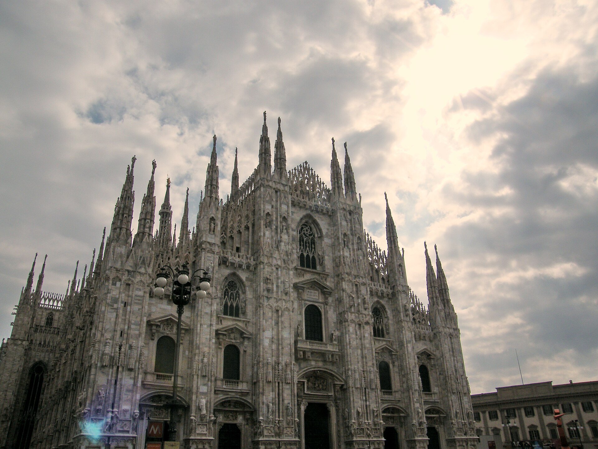 The marble front of Milan Cathedral seen at an angle against a clouded sky