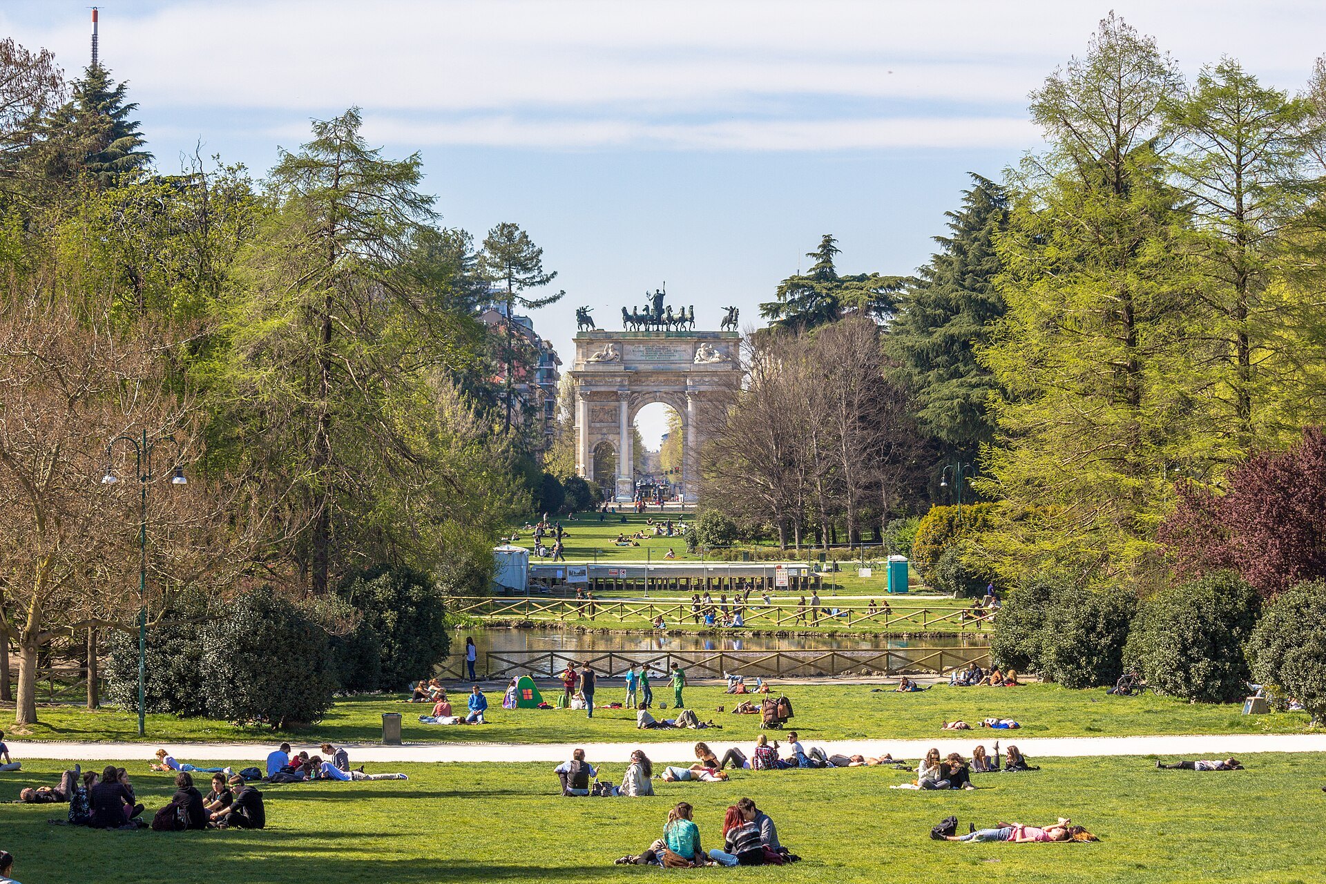 People lying on the grass in Parco Sempione with the Arco della Pace at the end of the lawn